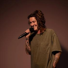 Irish comedian, Kyla Cobbler, performs stand-up comedy in front of a solid backdrop.