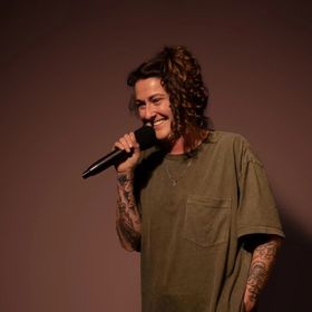 Irish comedian, Kyla Cobbler, performs stand-up comedy in front of a solid backdrop.