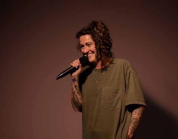 Irish comedian, Kyla Cobbler, performs stand-up comedy in front of a solid backdrop.