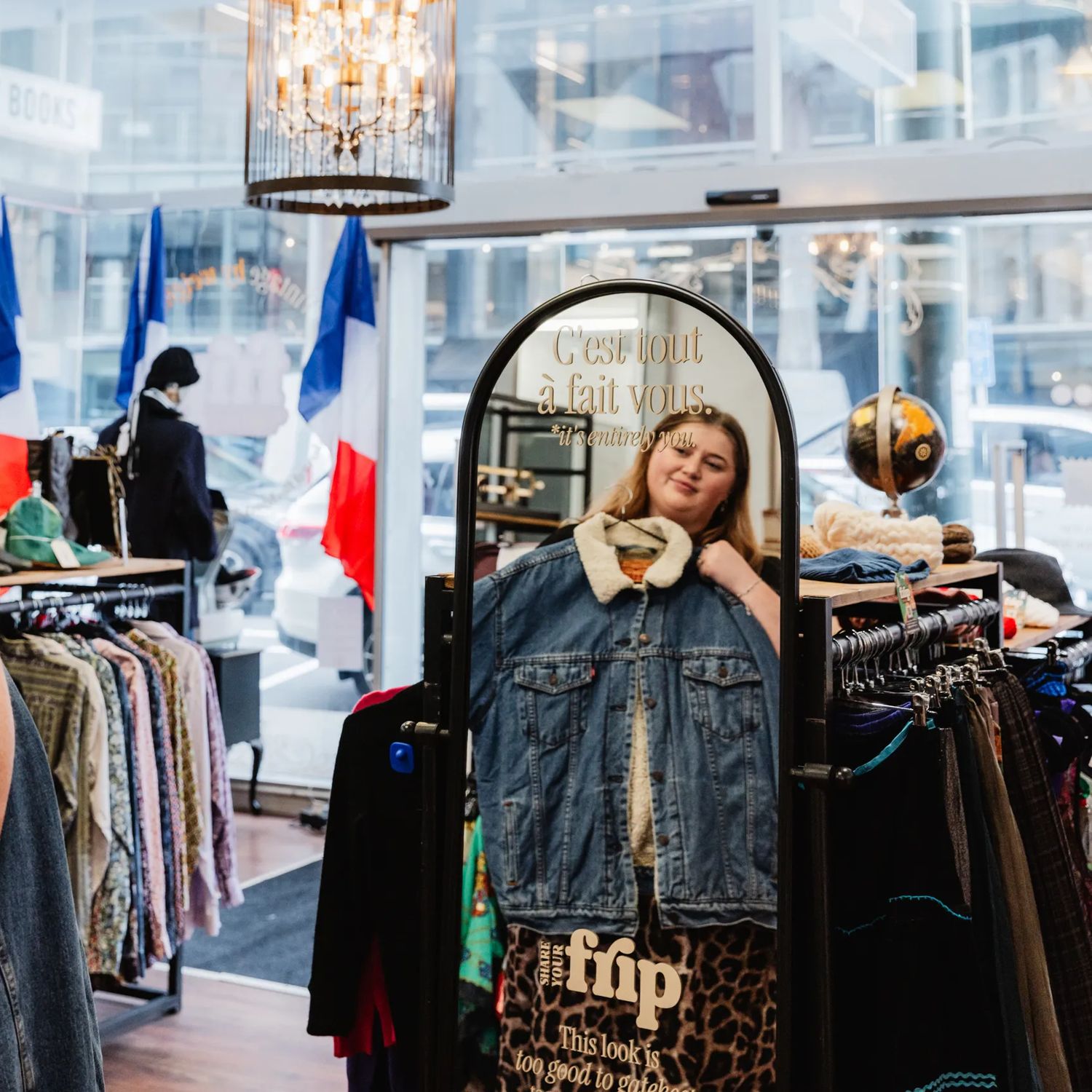 A person holding up an item of vintage clothing in a mirror inside Frip Vintage
