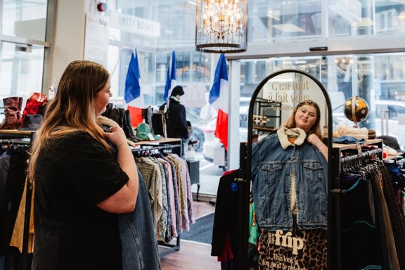 A person holding up an item of vintage clothing in a mirror inside Frip Vintage