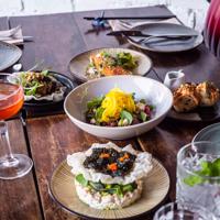 Five Asian-fusion dishes, a pink cocktail, dishes and utensils on a table at a restaurant.