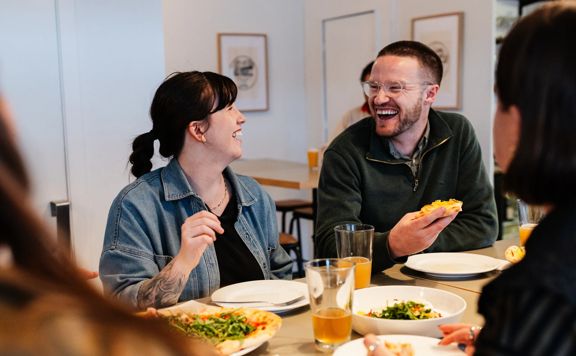 People gathered around a table sharing a meal at Station Kitchen in Ngaio, with plates of food and drinks in a bright café setting.