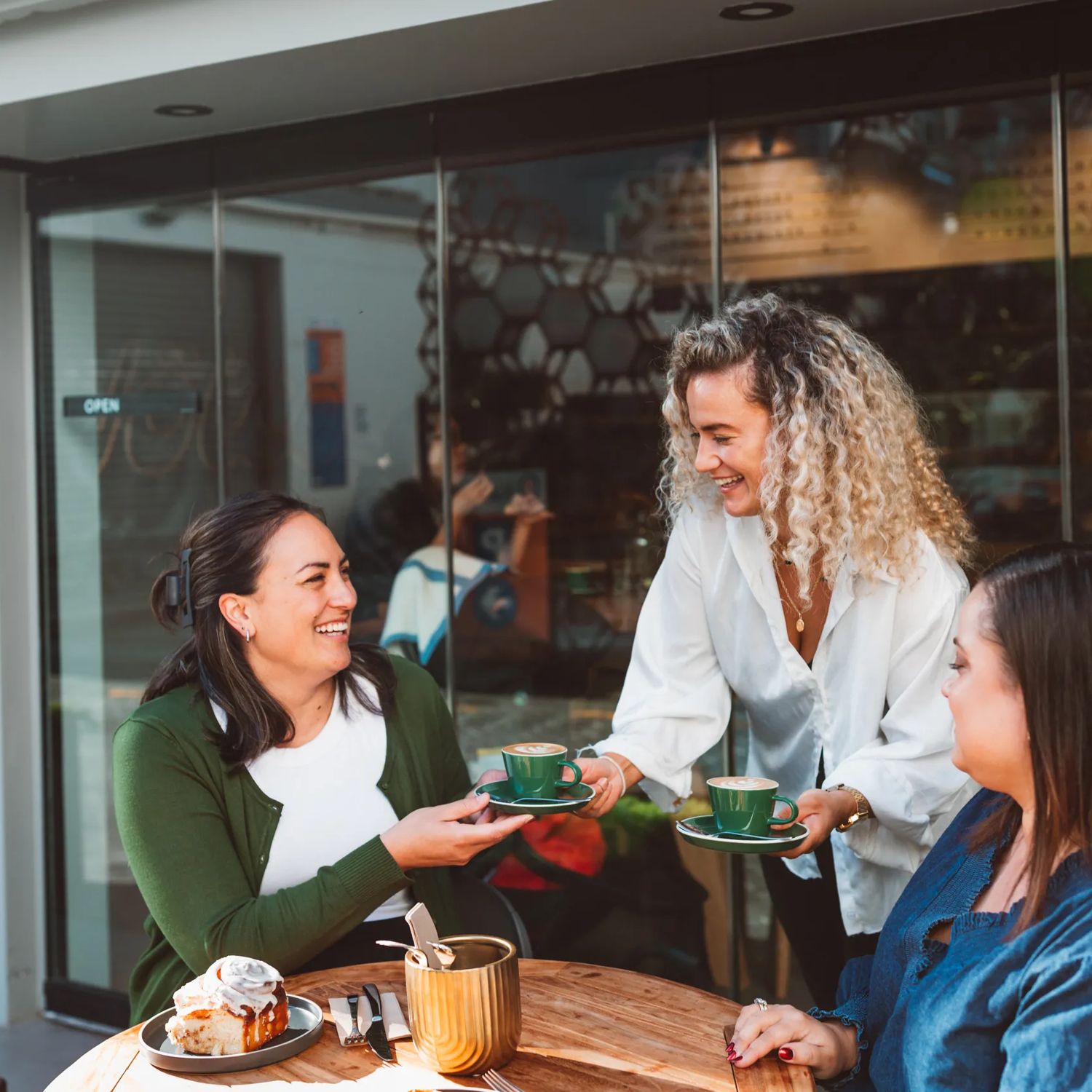 A server delivers a couple of coffees to friends dining on a patio.