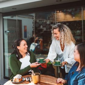 A server delivers a couple of coffees to friends dining on a patio.