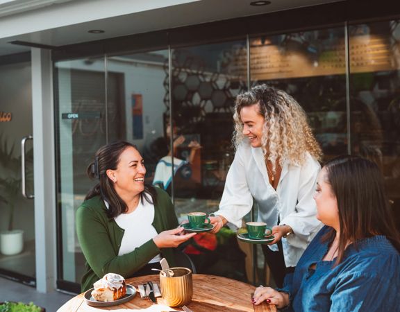 A server delivers a couple of coffees to friends dining on a patio.