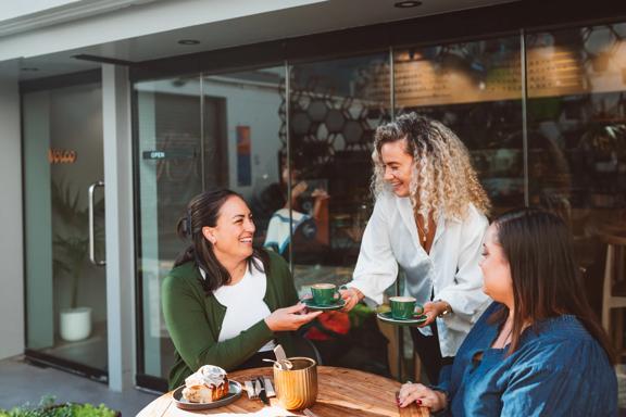 A server delivers a couple of coffees to friends dining on a patio.