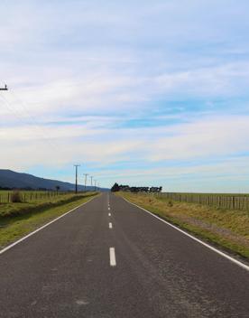 The rural Western Lake road, which connects the Remutaka Range to Lake Wairarapa, features lush green fields and mountains.