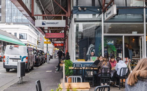 The exterior of Swimsuit Cafe on Dixon Street, people sit on tables outside the dark blue café.