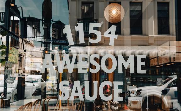 Text decal on the front window of 1154 Pastaria on Cuba Street saying “1154 Awesome Sauce”.