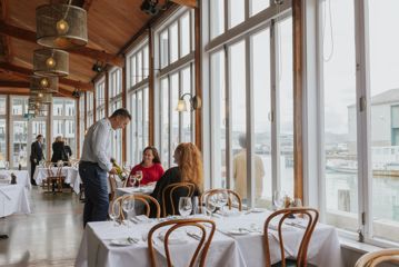 A waiter presents a bottle of white wine to a table of two by the window at Shed 5.