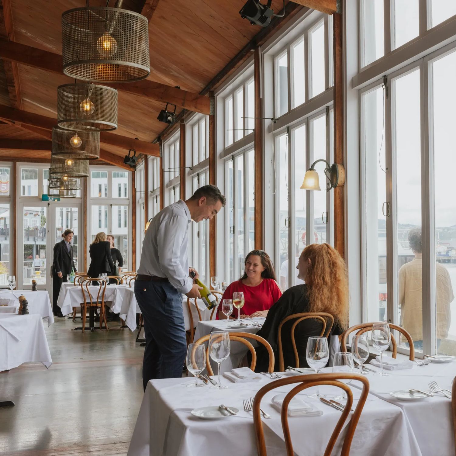 A waiter presents a bottle of white wine to a table of two by the window at Shed 5.