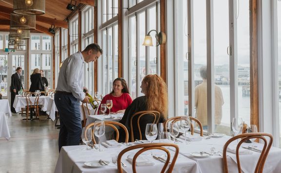 A waiter presents a bottle of white wine to a table of two by the window at Shed 5.