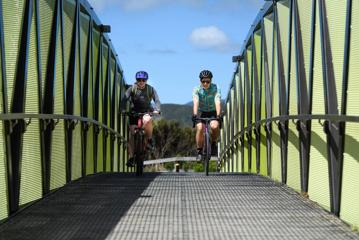 2 people on mountain bikes crossing a bridge on the Wainuiomata connector ride.