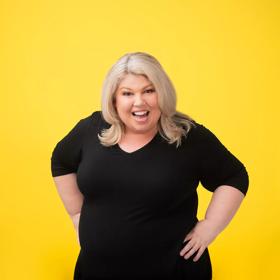 South African-Kiwi comedian, Urzila Carlson, poses and smiles in front of a coloured backdrop to promote her upcoming show at Wellington's The Opera House.
