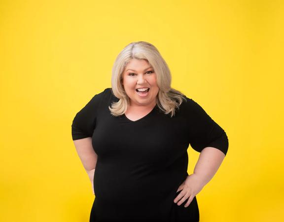 South African-Kiwi comedian, Urzila Carlson, poses and smiles in front of a coloured backdrop to promote her upcoming show at Wellington's The Opera House.