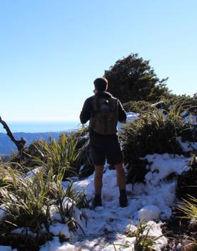 A hiker stands on a snowy summit on Kapakapanui Track looking out to the Tasman Sea.