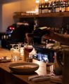 A staff member at highwater eatery pouring a glass of wine from behind the dimly lit bar.