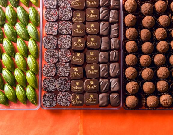 Three trays clear plastic of artisanal chocolates from Schoc Chocolates shop on a red-orange surface. 