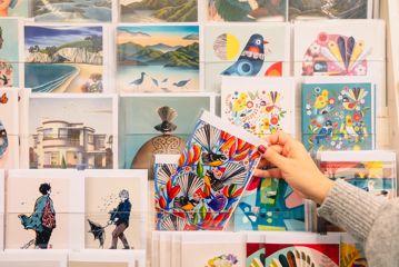 A hand pulls a celebration card out of a shelf full of other colourful cards.