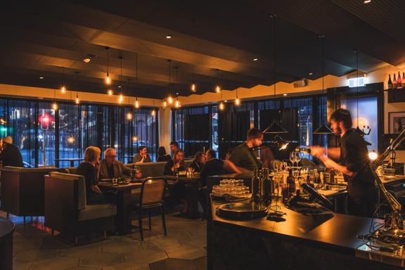 The interior of Plonk under low light, customers sit in the background enjoying their meals and bar staff serve drinks in the front.