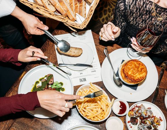 Looking down at a table of food inside Hippo, QT Wellington. Customers use a knife and fork to grab food.