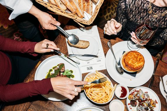 Looking down at a table of food inside Hippo, QT Wellington. Customers use a knife and fork to grab food.
