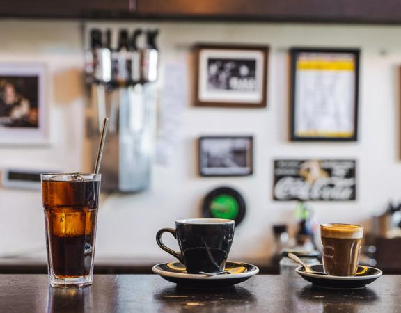 Three types of coffee, in different vessels, sit on the counter in Black Coffee in Newtown. Framed pictures are blurred on the walls in the background.