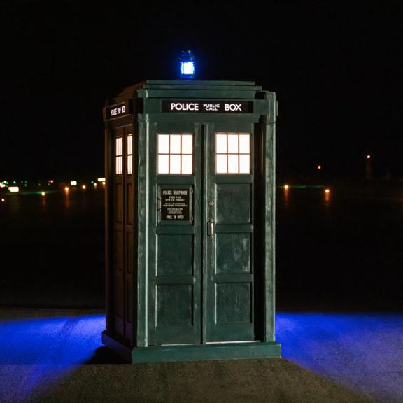 The 'TARDIS' blue police box was placed on the Wellington Airport runway in the dark. A blue light sits on top of the box illuminating the ground behind it.
