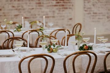 A close up of a banquet table setup with place settings and decor, three candles, a white table cloth and wooden chairs at the Whisky and Wood event venue in Wellington Central.