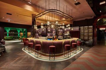 A swanky hotel bar with colourful art deco decor and low lighting.