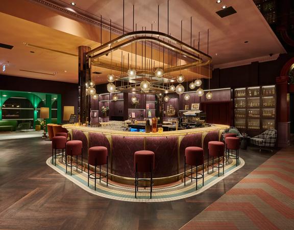 A swanky hotel bar with colourful art deco decor and low lighting. 