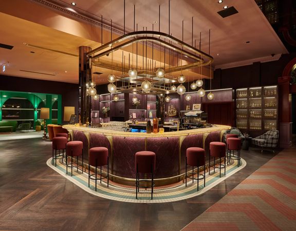 A swanky hotel bar with colourful art deco decor and low lighting.