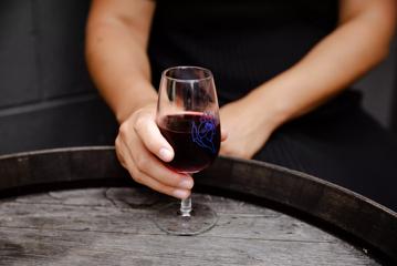 Close up of persons hand holding a glass on wine, with Ascots logo on the glass.