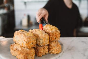 A person using tongs to place a cheese scone onto a stack on a marble plate at Floriditas, a restaurant on Cuba Street in Te Aro, Wellington.