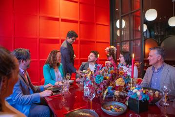 Six conference attendees enjoy dinner and drinks at Lola Rouge Restaurant & Bar at Naumi Hotel in Wellington. A big colourful bouquet centrepiece is on the red table in a red room.