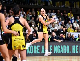 Netballer Whitney Souness of the Pulse jumps on the court with the netball in her hand. She wears the yellow and black team dress and the crowd is behind her.