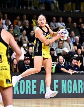 Netballer Whitney Souness of the Pulse jumps on the court with the netball in her hand. She wears the yellow and black team dress and the crowd is behind her.