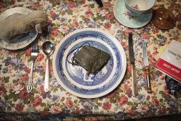 A table setting on a floral tablecloth with a plush bunny on the side plate, utensils, a teacup and a New Zealand greenstone, pounamu, placed in the centre plate.