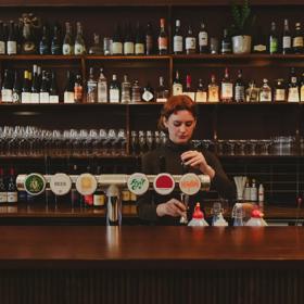 The Bar staff behind the bar at The Ram pouring craft beer. Theres a large shelf of wine and spirits bottles behind them.