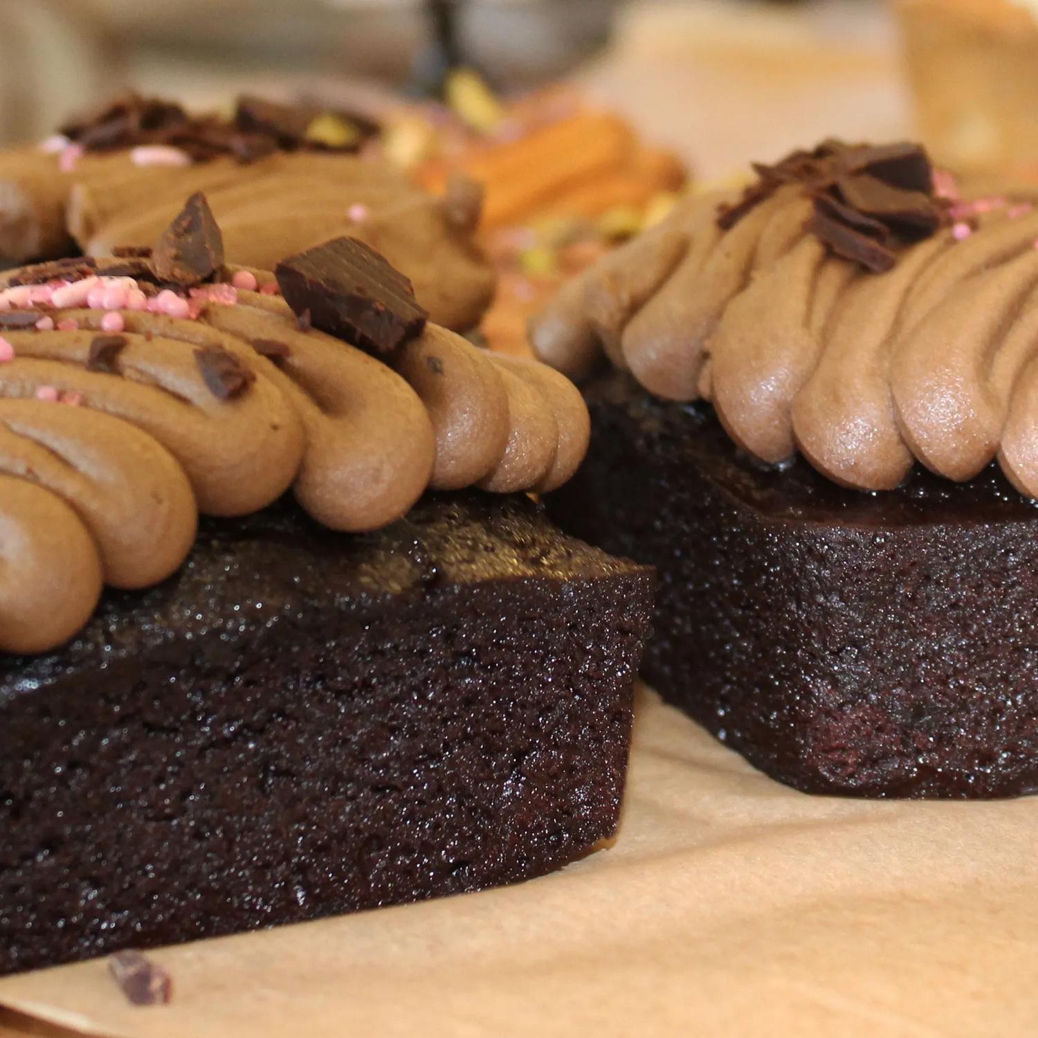 Several chocolate cakes with squiggles of chocolate icing sit on a wooden board.