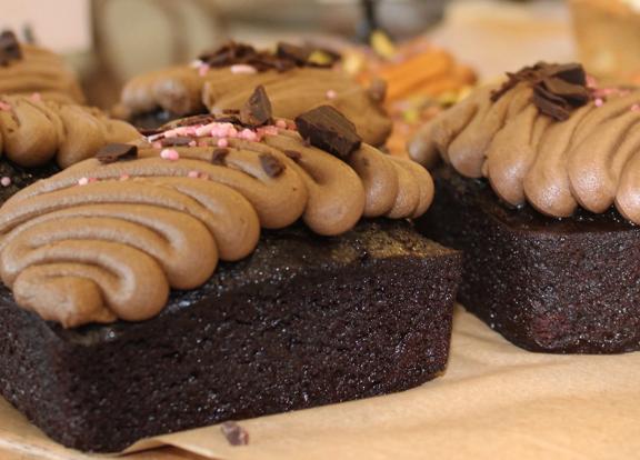 Several chocolate cakes with squiggles of chocolate icing sit on a wooden board.