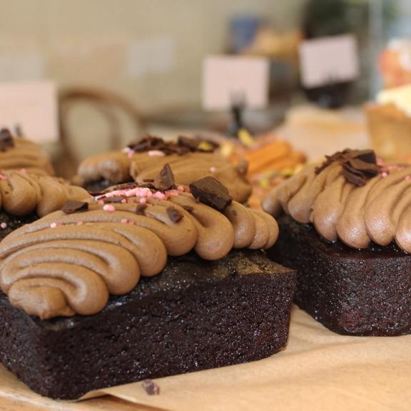 Several chocolate cakes with squiggles of chocolate icing sit on a wooden board.