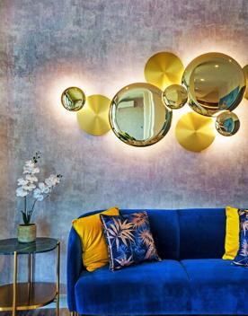A Dark blue sofa with gold cushions, gold side table, and yellow light fixture inside The Sebel.