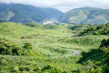 Three cyclists ride on a paved path in a lush green valley.