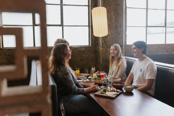 Four friends sit in a booth by a window, enjoying food and drinks at Chow in Wellington.
