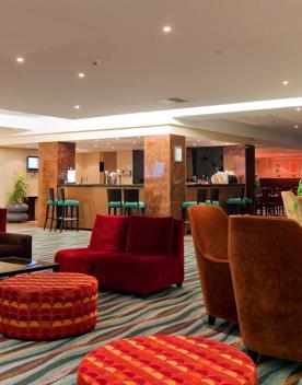 The Copthorne Hotel lobby, orange and brown armchairs surround tables, and a bar can be seen in the background.