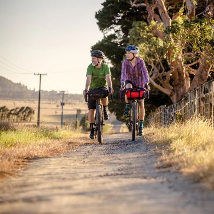 Two people riding bicycles side by side on a farm road.