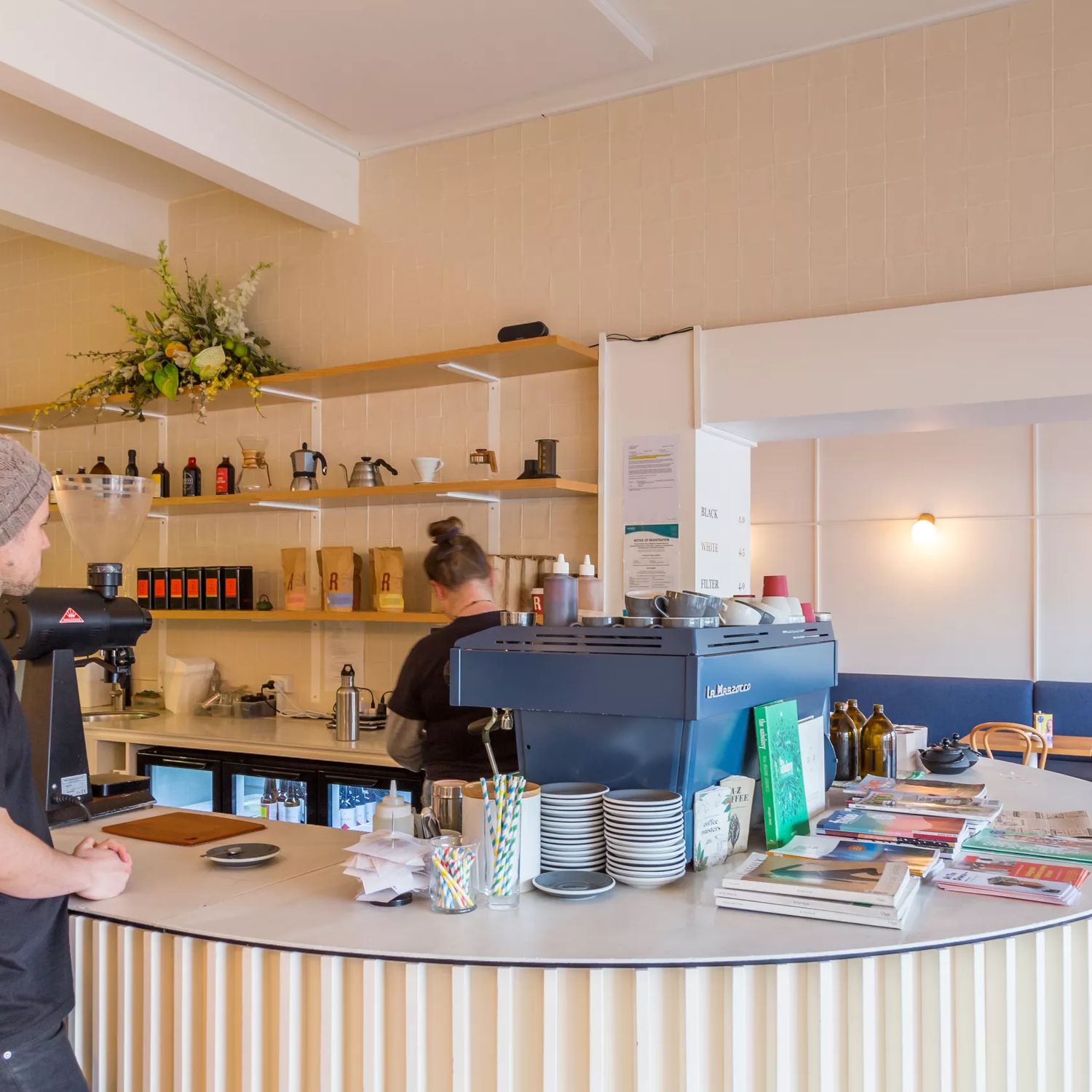 Interior shot of Comes and goes, with a customer waiting to order, barista making coffee and customers in the back sitting at booths.