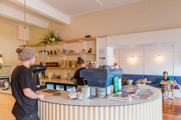 Interior shot of Comes and goes, with a customer waiting to order, barista making coffee and customers in the back sitting at booths.